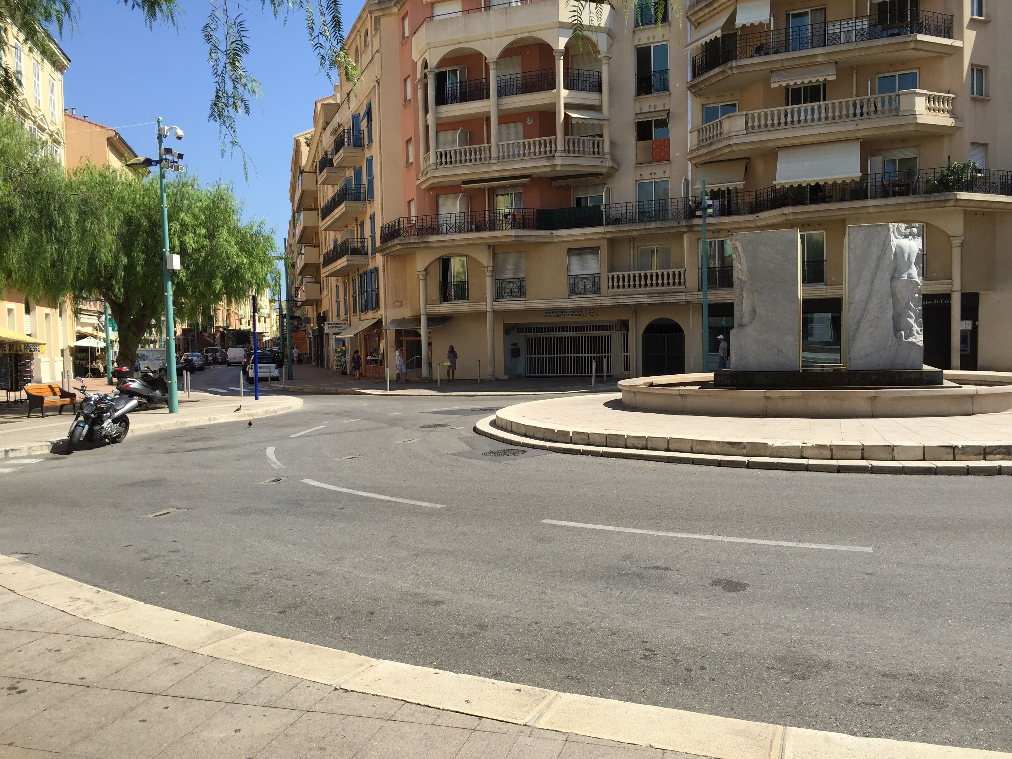 A multi-story building with balconies, a roundabout, and a parked motorcycle.
