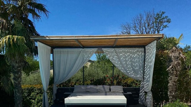 A poolside bedroom with a bed under a canopy, surrounded by a pool and greenery.