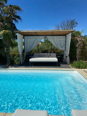 A poolside bedroom with a bed under a canopy, surrounded by a pool and greenery. - Charming villa with jaccuzi (Saint-Dézéry)