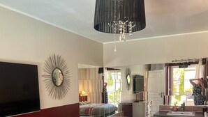 A spacious bedroom with a large bed, a TV, a chandelier, and a bathroom with a bathtub and sink.
