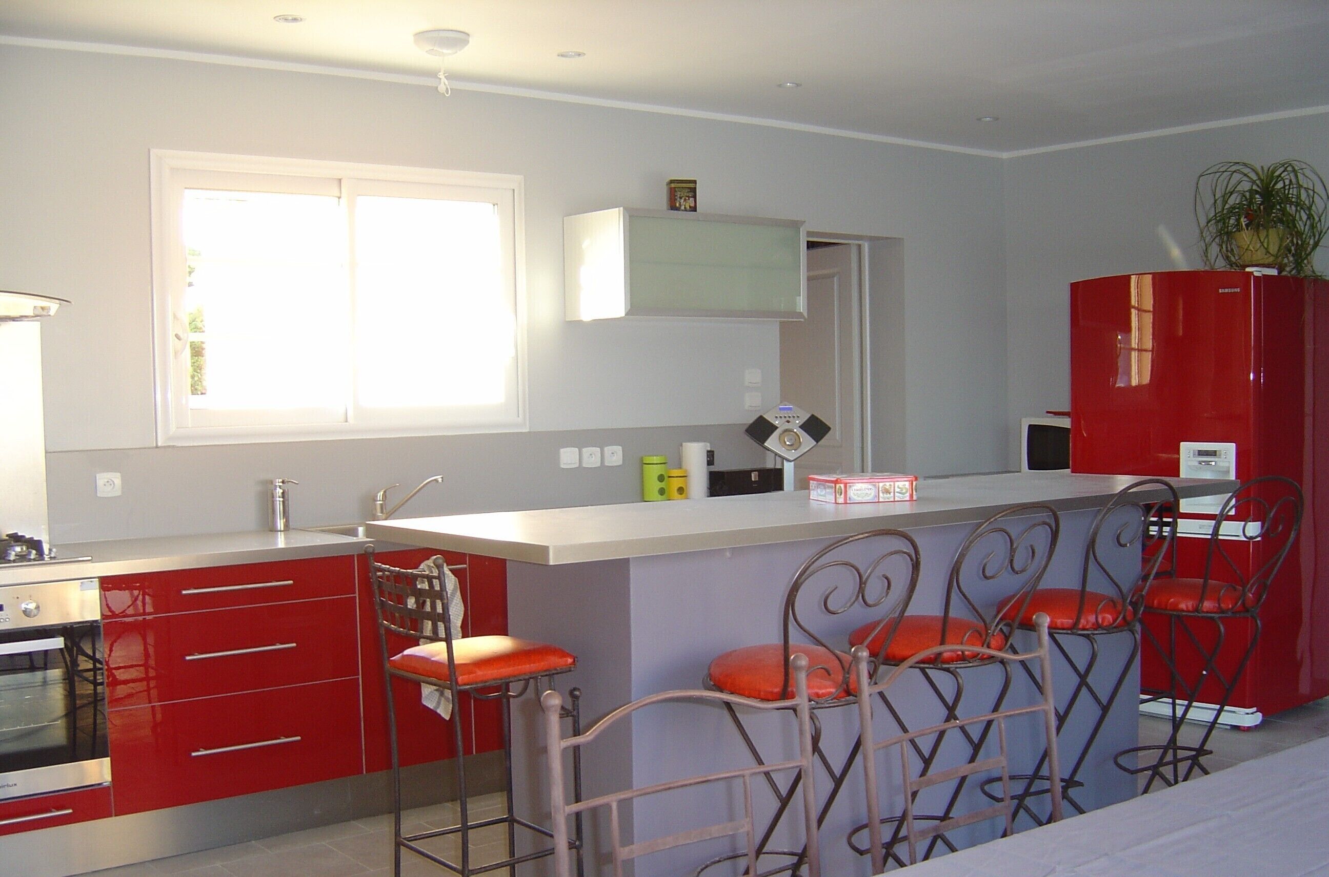 A modern kitchen with red cabinets, a white countertop, and a built-in island with bar stools.