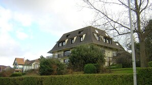 Une grande maison à deux étages, dotée d’un toit à forte pente, de nombreuses fenêtres et d’un balcon.