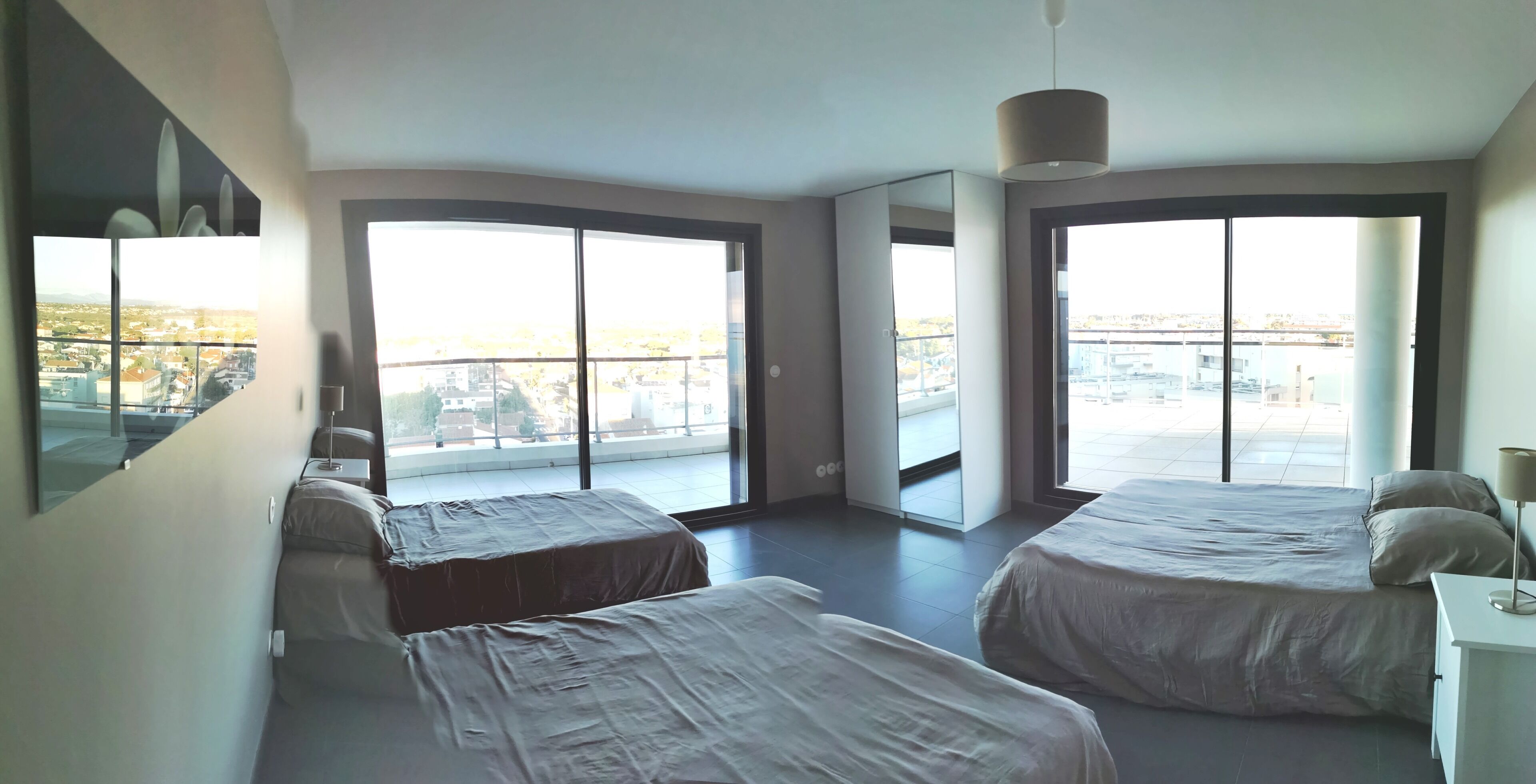 A modern hotel room with two beds, large windows, and a city view.