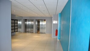 En rummelig gang med en blå accentvæg, en brandslukker og et elevatorområde med metalvægge.
