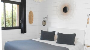 Ein Schlafzimmer mit einem großen Bett, einer hängenden Leuchte, einem wandmontierten Spiegel und einem Fenster mit Vorhängen.
