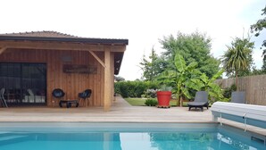 Eine Holzterrasse mit Pool, Liegestühlen und einer überdachten Sitzgelegenheit mit Blick auf den Pool.
