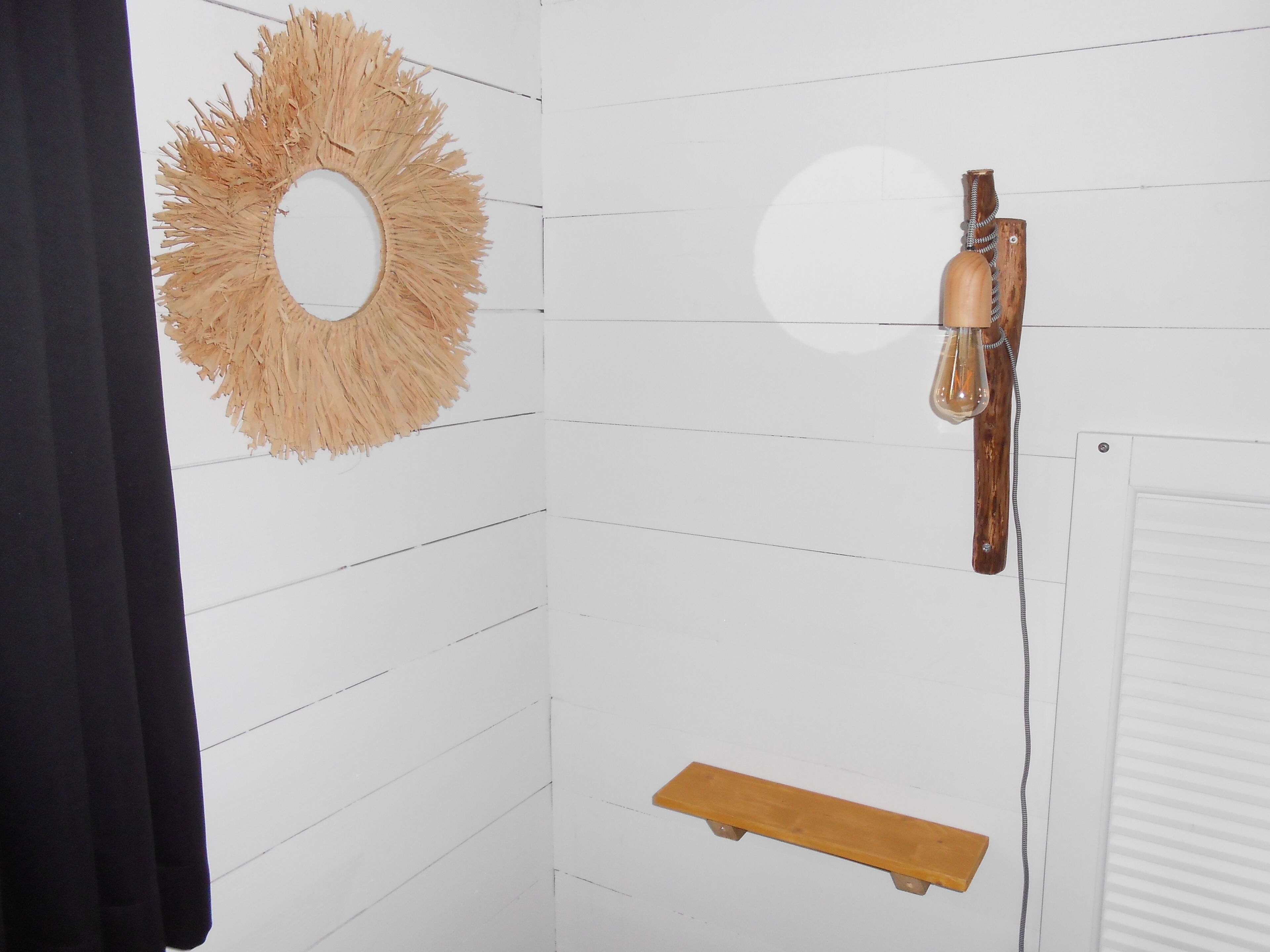 Ein Badezimmer mit weißen Fliesen, einem Holzregal, einem Handtuchhalter und einem runden Spiegel.