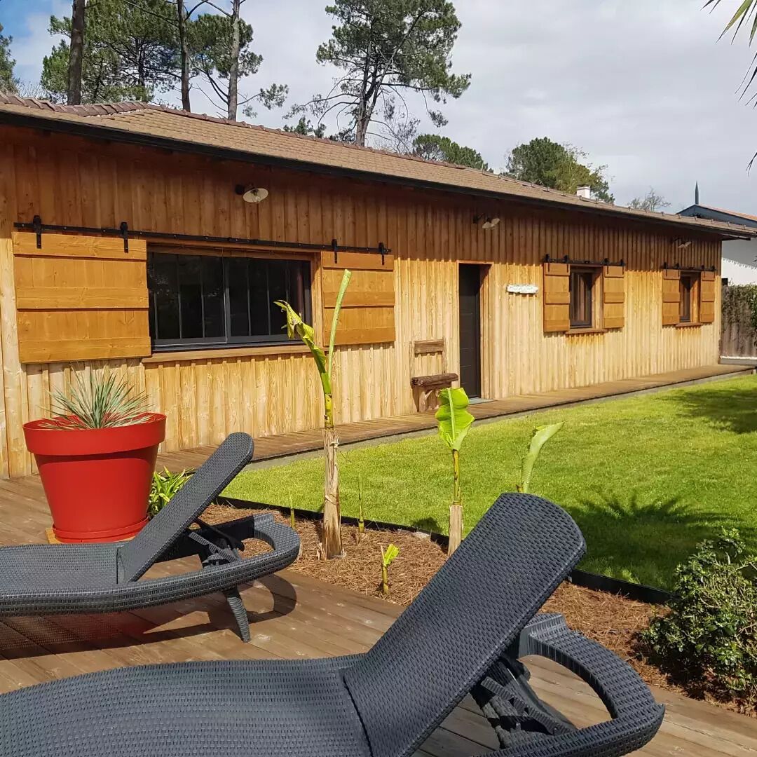 A wooden house with a deck, two lounge chairs, and a small garden.