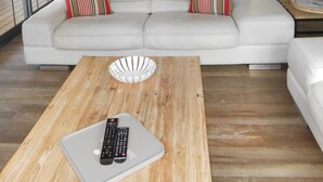 Ein geräumiger Wohnbereich mit einem weißen Sofa, einem Holztisch und einer Küche im Hintergrund.