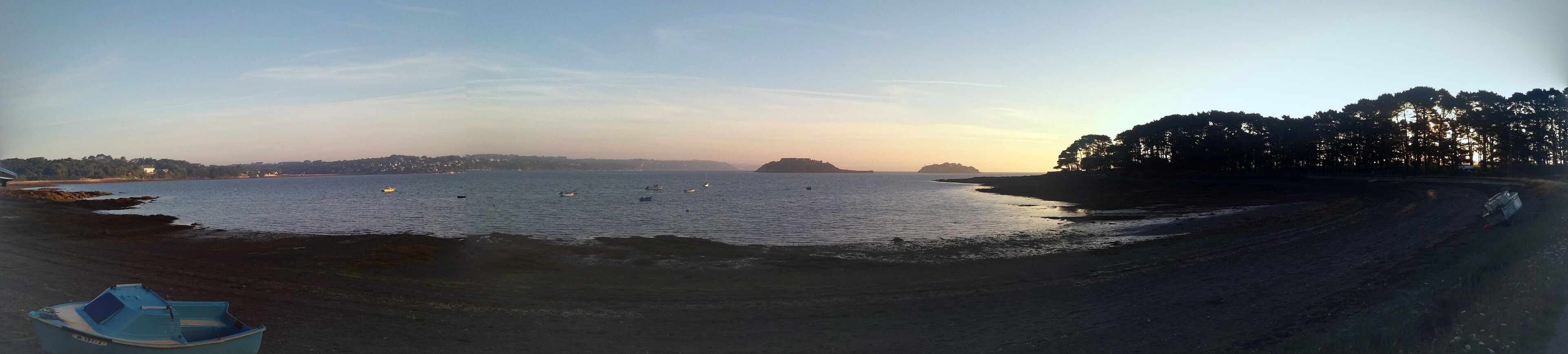 Une plage avec des bateaux, un ciel dégagé et une terre lointaine à l’horizon.