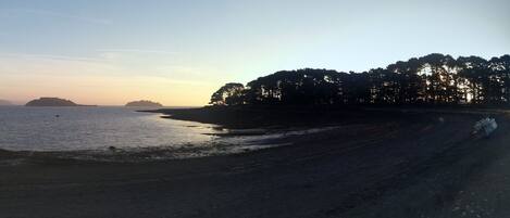 Une plage avec des bateaux, un ciel dégagé et une terre lointaine à l’horizon.