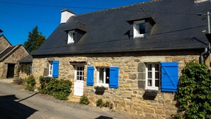 A stone building with a dark roof, multiple windows with blue shutters, and a small door. - Old stone house between Crozon and Camaret (sea 200m) (Crozon)