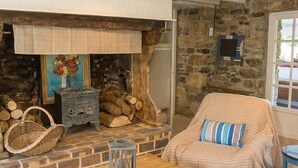 A cozy room with a stone fireplace, a bed with striped bedding, a wicker basket, and a small table with a candle. - Old stone house between Crozon and Camaret (sea 200m) (Crozon)