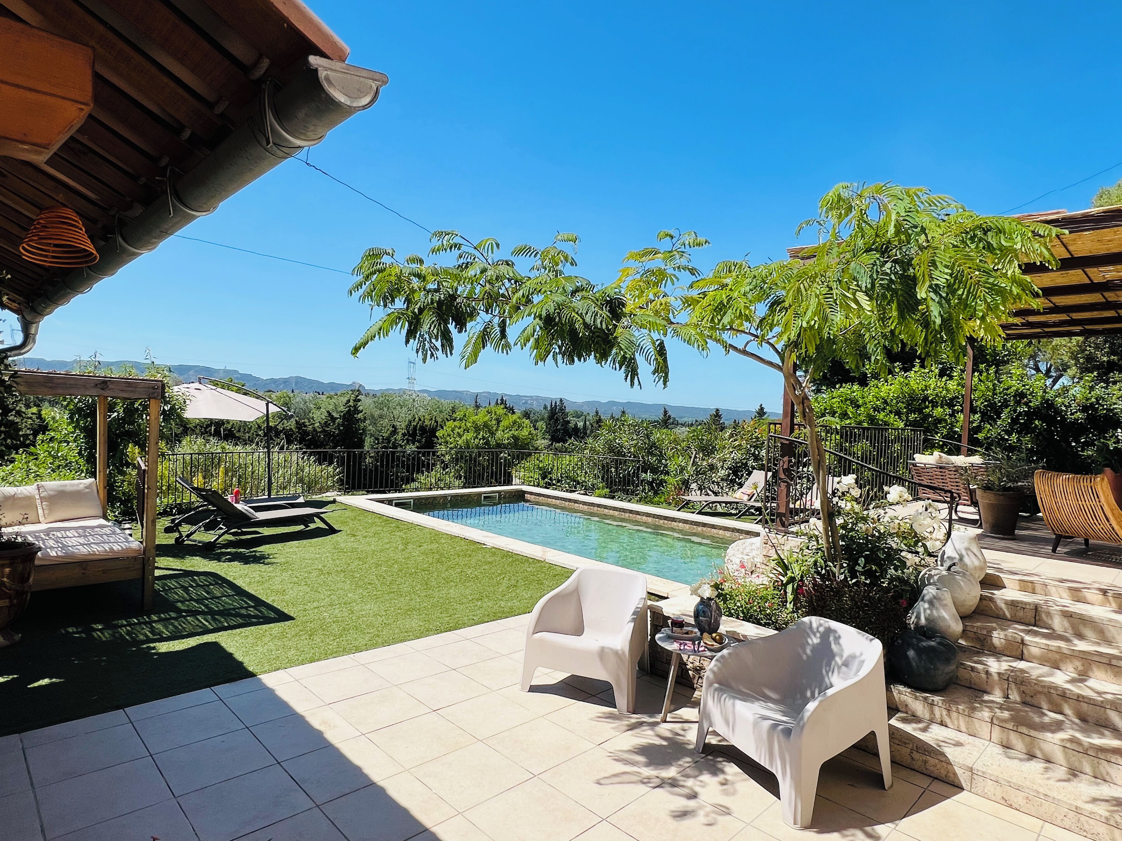Un espace piscine offrant une vue sur les montagnes, entouré de verdure et agrémenté de mobilier d’extérieur.