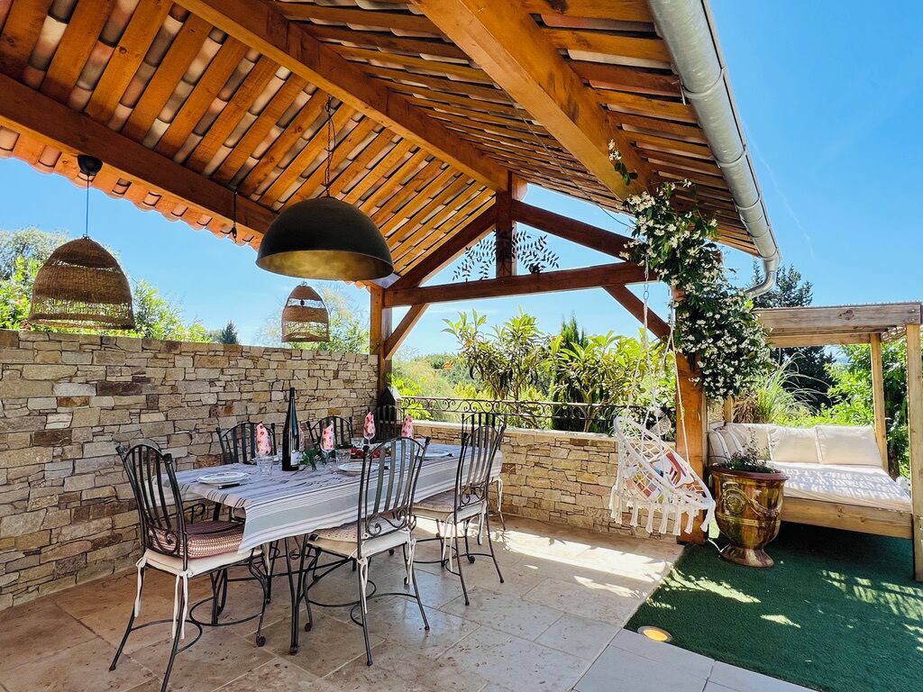 Une terrasse extérieure agrémentée d’une pergola en bois, de murs en pierre et d’une table à manger pouvant accueillir six personnes.