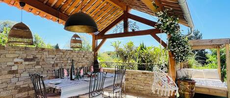 Une terrasse extérieure agrémentée d’une pergola en bois, de murs en pierre et d’une table à manger pouvant accueillir six personnes.