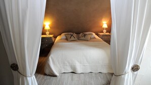Een slaapkamer met een bed, twee nachtkastjes met lampen en witte gordijnen.
