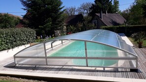 A covered swimming pool with a clear roof, surrounded by a wooden deck and lush greenery. - An old house located on an apple orchard (Savignac-Lédrier)