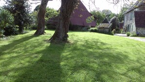 A well-maintained lawn with two large trees and a red-roofed building in the background. - Old house located on an apple-red fruit farm (Savignac-Lédrier)