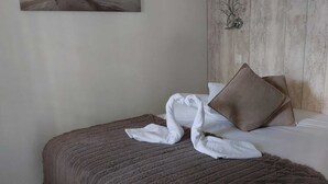 Een net opgemaakt bed met een bruine deken en witte kussens, een schilderij van een strandtafereel aan de muur, en een klein decoratief object met de tekst "LOVE" op het hoofdeinde.
