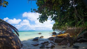 Ein tropischer Strand mit klarem türkisblauem Wasser, großen Felsen und üppiger Vegetation.