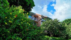 Ein Gebäude mit Balkon, umgeben von üppigem Grün und blühenden Pflanzen.