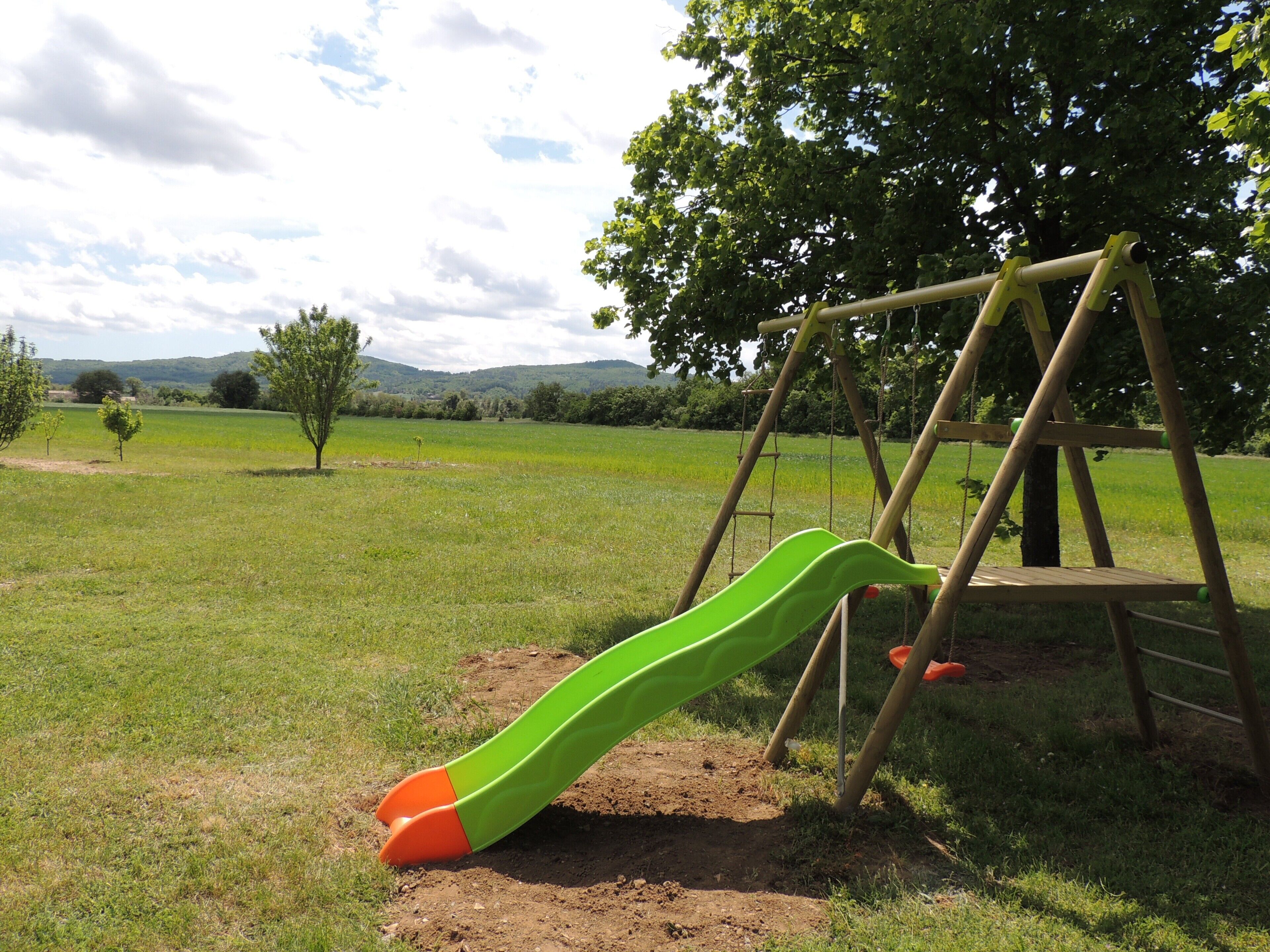 Un parque infantil con un tobogán verde y un columpio de madera en un campo cubierto de césped.
