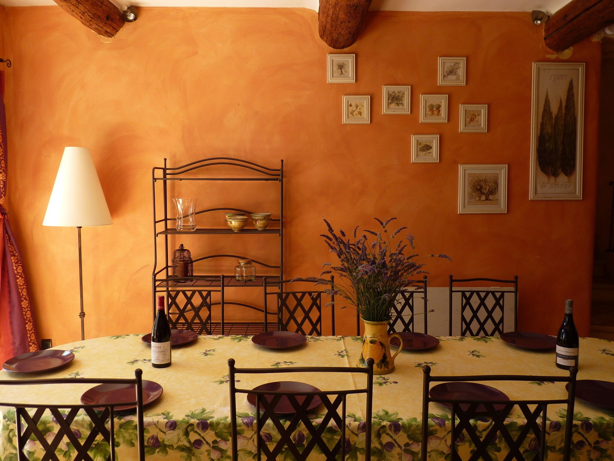Een eethoek met een tafel voor vier personen, omringd door stoelen, een metalen schap met servies, en een vaas met bloemen.