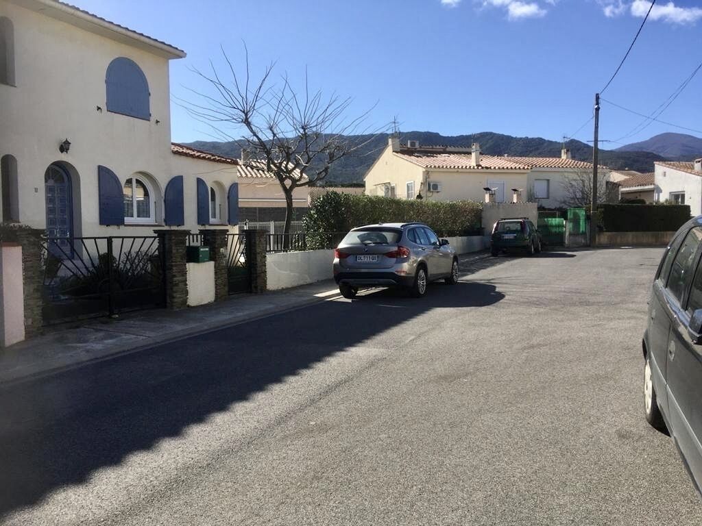 Eine Wohnstraße mit Häusern, parkenden Autos und blauem Himmel.