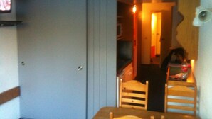 A room with a wooden dining table and chairs, a television mounted on the wall, and a door leading to another room. - Charming studio in Arcs 1800, at the foot of the slopes, in the heart of the village (Bourg-Saint-Maurice)