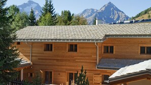 Un chalet en bois doté de nombreuses fenêtres, d’un toit en pente et offrant une vue sur les montagnes.