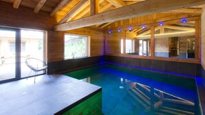 Une piscine intérieure avec des poutres en bois, une chaise et une vue sur l’extérieur.