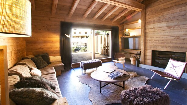 L’intérieur chaleureux d’un chalet en bois comprend un canapé, un pouf et des fauteuils, une cheminée et une grande fenêtre qui laisse entrer la lumière naturelle.