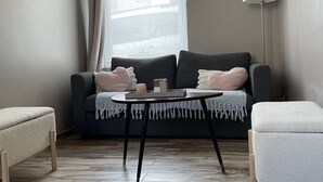 En moderne stue med en grå sofa, et lille rundt bord og en gulvlampe.