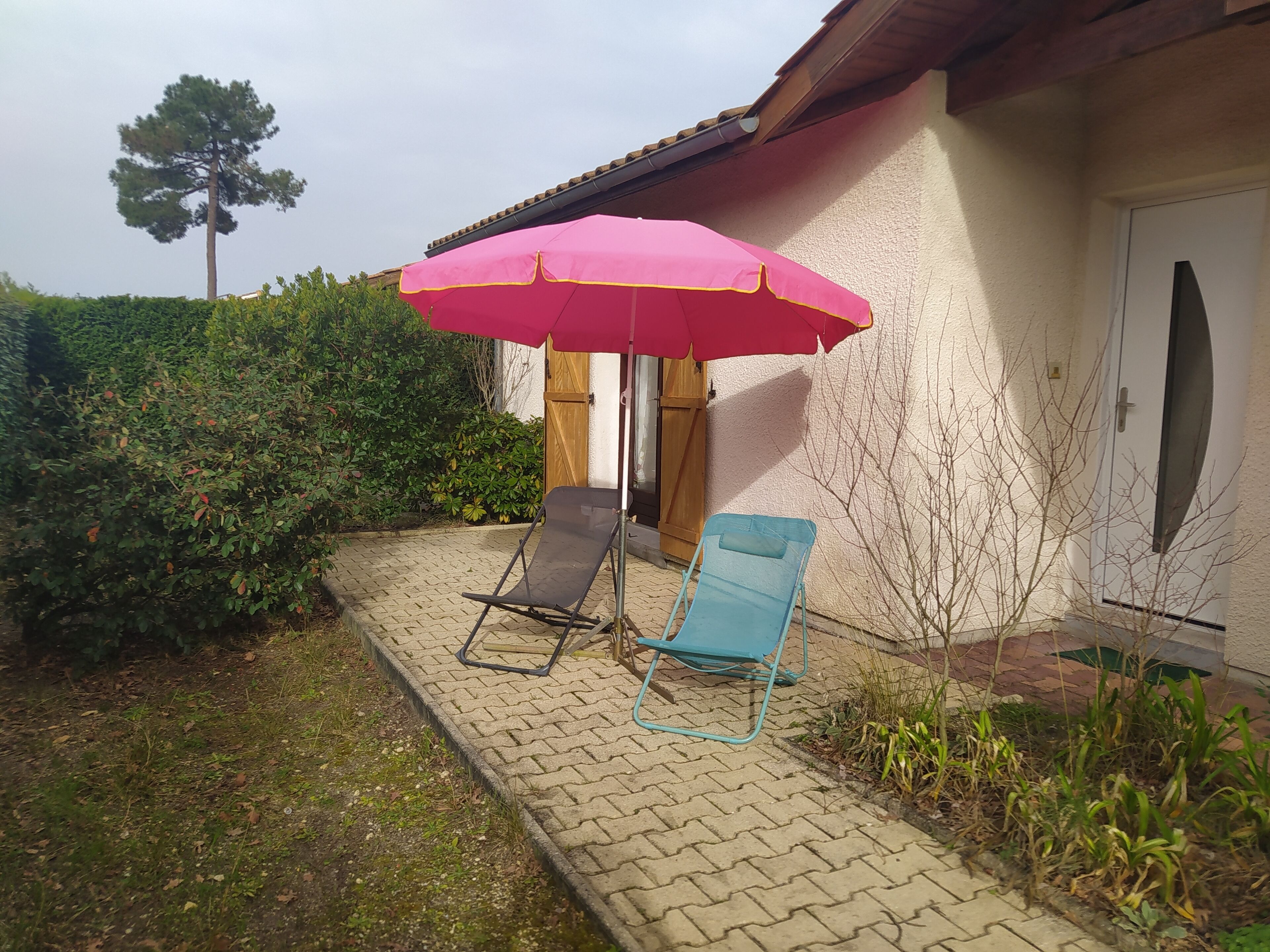 Un patio con dos sillones de descanso, un paraguas rosa y un seto.