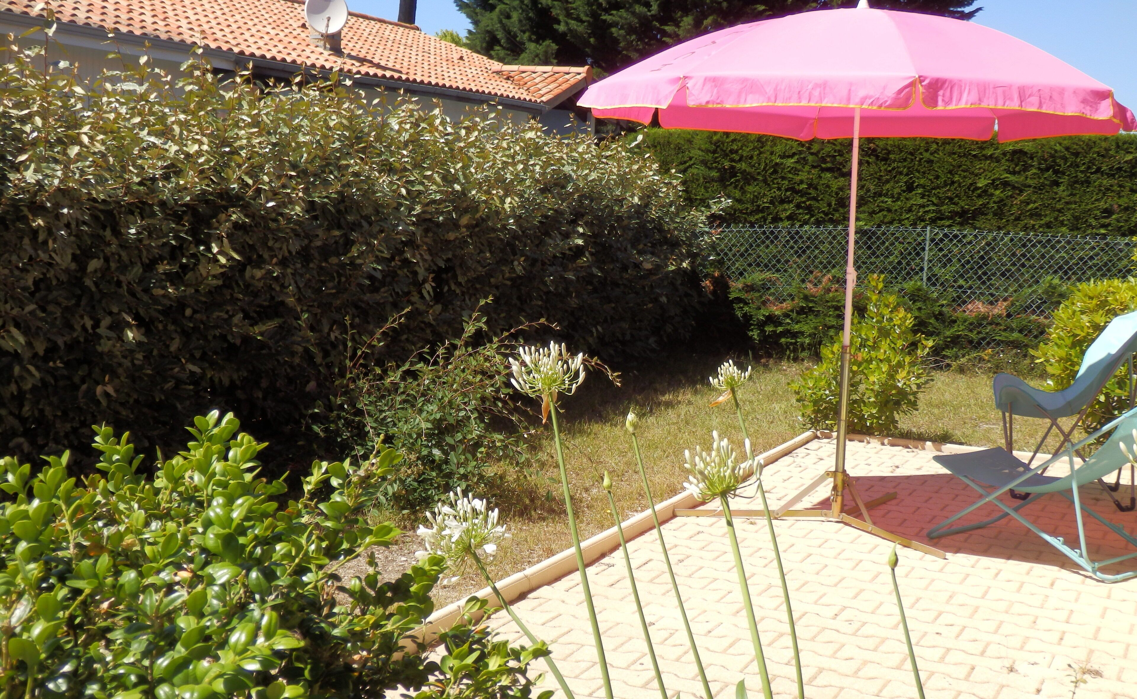 A patio area with a pink umbrella, a chain-link fence, and a blue chair.