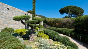 A well-maintained garden with a variety of shrubs and trees, a stone wall, and a clear blue sky. - Magnificent villa with breathtaking views of Palombaggia beach Private sea access (Porto-Vecchio)