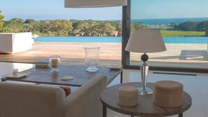 A modern living room with a sofa, a round table with a lamp, and a view of a pool and ocean. - Magnificent villa with breathtaking views of Palombaggia beach Private sea access (Porto-Vecchio)