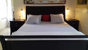 Une chambre d’hôtel avec un grand lit, deux tables de chevet, une commode, un tableau au mur et une fenêtre avec des rideaux.