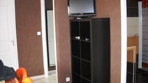 A room with a television on a black stand, a door, and a small table with a chair. - Pavillon Hourtin-ville, near the lake (Hourtin)