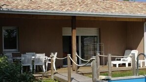 A pool area with a covered seating area, white plastic chairs, and a rope barrier. - Pavillon Hourtin-ville, near the lake (Hourtin)