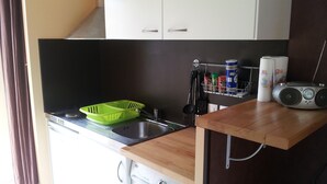A compact kitchen with a washing machine, a sink, and a radio on the countertop. - Pavillon Hourtin-ville, near the lake (Hourtin)