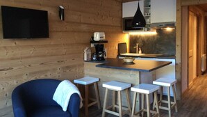 Een gezellige keuken met houten wanden, een flatscreen televisie, een koffiezetapparaat en een magnetron. Drie krukken en een blauwe stoel zijn aanwezig.