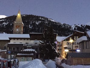 Une ville enneigée, avec un clocher d’église imposant, un hôtel et un bar.