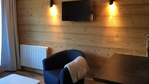 Een kamer met houten paneelwanden, een flatscreen televisie boven een donkerblauwe fauteuil en twee wandlampen.