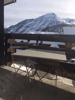 Une table et des chaises en bois sont disposées sur un balcon offrant une vue sur la montagne.