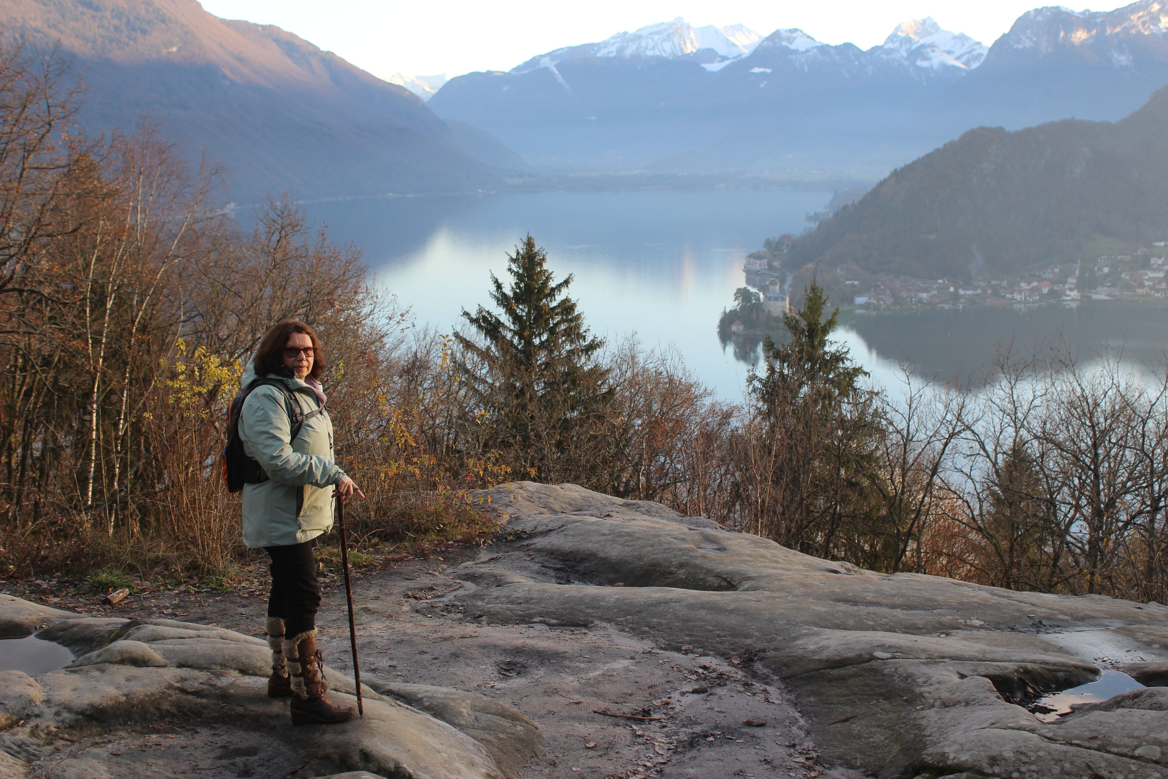 Une personne se tient debout sur un promontoire rocheux, surplombant un lac, avec des montagnes en arrière-plan.