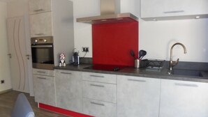 A modern kitchen with stainless steel appliances, a red accent wall, and a built-in sink. - Provence, its lavender, the song of the cicadas, the sun ... Let yourself be seduced ... (Carpentras)