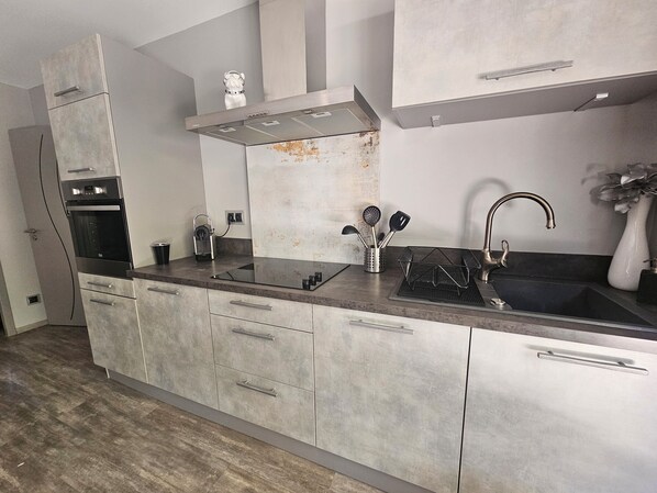 A modern kitchen with a stainless steel range hood, a built-in oven, a sink with a faucet, and a countertop with a utensil holder. - Provence, its lavender, the song of the cicadas, the sun ... Let yourself be seduced ... (Carpentras)