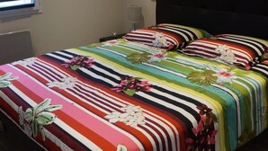 A bedroom with a bed covered in a floral-patterned bedspread, a black headboard, and a wall-mounted light fixture. - Provence, its lavender, the song of the cicadas, the sun ... Let yourself be seduced ... (Carpentras)